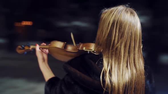 joyful girl in a black half-length coat is holding a violin in her hands and playing on it