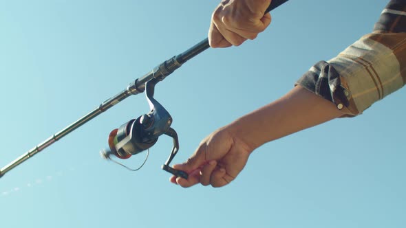 Low Angle View of Black Male Hands Holding Rod and Turning Fishing Reel