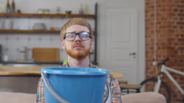 Man Holding Bucket While Water Leaking From Ceiling in Living Room