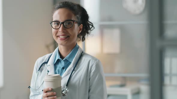 Portrait of Cheerful Female Doctor Holding Coffee and Smiling at Camera