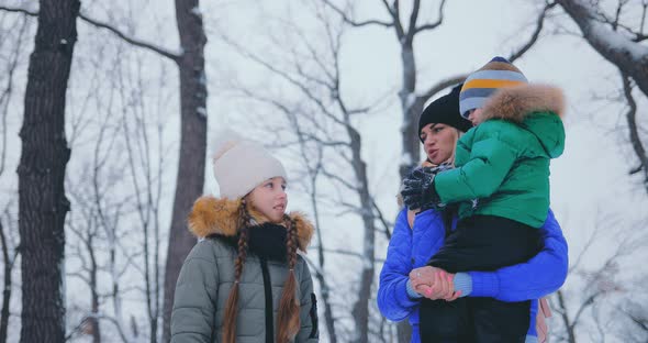 Young Mother Talks with Children on a Walk in the Winter