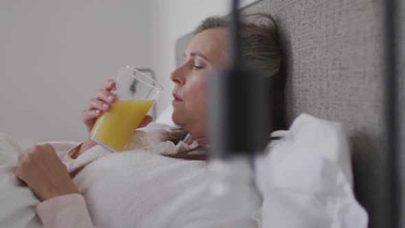 Sick woman drinking juice while lying in bed at home