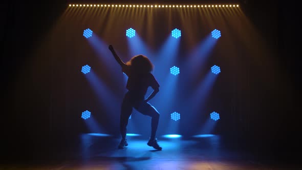 A Young Slender Girl with Lush Hair Dances Jazz Funk on a Background of Blue Lights. Professional