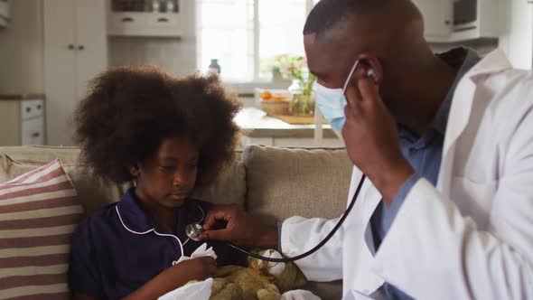 African american doctor wearing face mask using stethoscope to treat a sick girl at home
