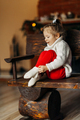 Baby is sitting on a bench against the background of the fireplace and putting on warm socks - PhotoDune Item for Sale