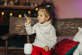 A cheerful baby is drinking hot chocolate on a bench by the fireplace. Christmas mood - PhotoDune Item for Sale