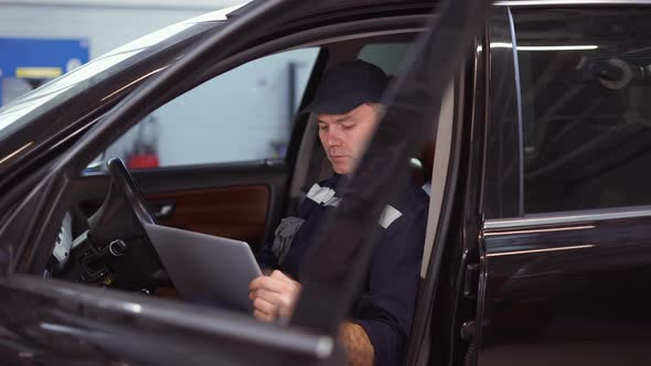 Car Mechanic Working on Laptop in Auto Repair Service Inside the Car