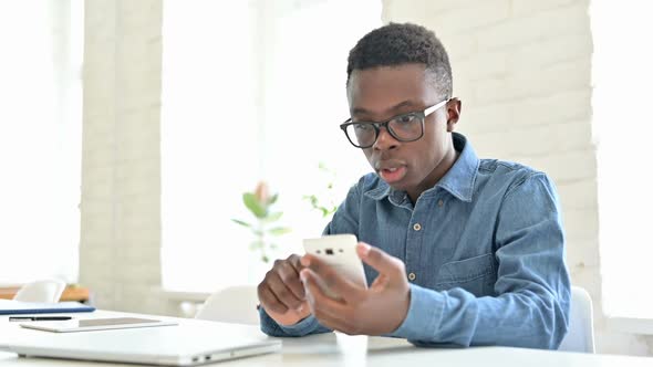 Young African Man Celebrating Success on Smartphone in Office