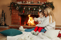 Mother and daughter hugging and warming up on a winter evening by the fireplace for Christmas - PhotoDune Item for Sale