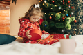 Little girl opens a Christmas present near the Christmas tree - PhotoDune Item for Sale