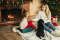 Happy mom and daughter play with their dachshund dog on the floor by the fireplace and Christmas - PhotoDune Item for Sale