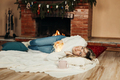 A charming young woman lies on a rug by the fireplace on Christmas Eve - PhotoDune Item for Sale