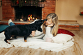 Woman playing with a dog sitting on the floor by the fireplace, on Christmas Eve - PhotoDune Item for Sale