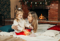 Mom and daughter are playing with Christmas garlands on the floor by the fireplace - PhotoDune Item for Sale