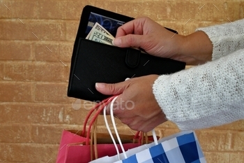 purchase, spend, shop, buy. Money, dollars, bills, cash, finances, expenses, paper money, green backs, 20 dollar bill, Pulling money out of a wallet while holding shopping bags to make a cash purchase.
