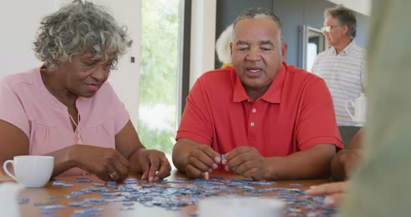 Happy senior diverse people playing puzzle at table at retirement home