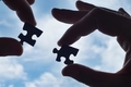 Jigsaw puzzle pieces held between fingertips with blue sky background. - PhotoDune Item for Sale