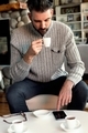 Man drinking a tiny cup of espresso coffee while scrolling on phone screen in cafe. - PhotoDune Item for Sale