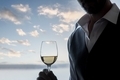 Man holding glass of white wine with cloudy blue sky.  - PhotoDune Item for Sale