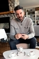 Man wearing a cozy grey sweater sitting at small table enjoying espresso coffee scrolling on phone. - PhotoDune Item for Sale