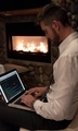 Working overtime, man sitting with laptop in lap writing computer code at night with fireplace. - PhotoDune Item for Sale