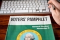 Voters' Pamphlet point of view on desk with keyboard and hand. - PhotoDune Item for Sale