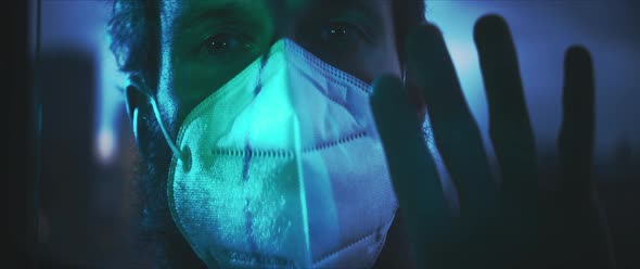 Man in a medical mask putting his hand on a window