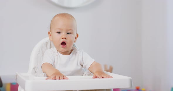 Portrait of Young Baby in White High Baby Chair White Walls on Background