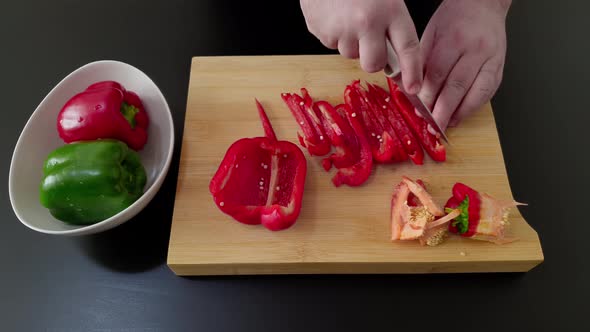 Male Hands Slicing Red And Green Bell Pepper On A Wooden Chopping Board - high angle shot, close up