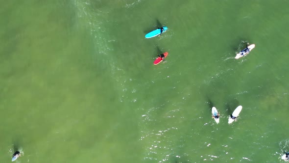 A top down drone shot over surfers waiting for a wave which rolls in & sprays a beautiful mist. The