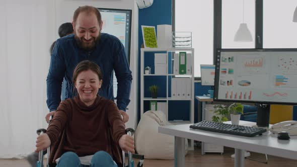 Man Employee Taking Break Pushing Wheelchair with His Paralysed Colleague