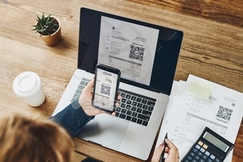 canning QR code from invoice to make payment using fast secure payment system and smartphone code reader. Business woman paying bills using express payment technology. Female using mobile phone and laptop. Paying expenses online. QR scanner. Making payment