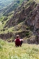 A young blond boy is sitting on the green grass and looking at the mountains. - PhotoDune Item for Sale