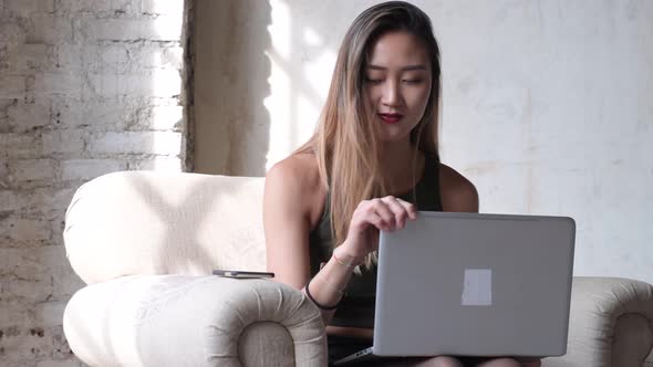 young woman sitting armchair office interior using laptop computer and smart phone