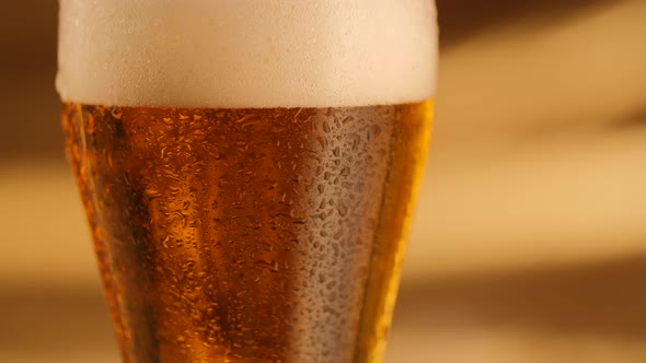 Closeup of Rotating Fresh Beer with Abstract Golden Background and Drops on Glass