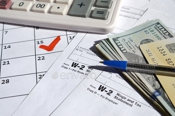 on dollar bills, calculator and pen on calendar page with marked 15th April. Tax period concept. IRS Internal Revenue Service
