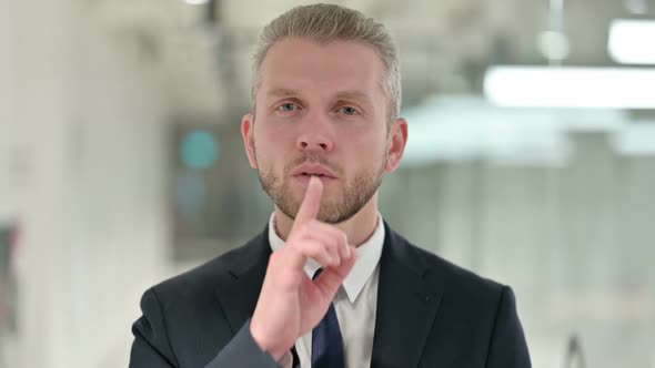 Portrait of Serious Young Businessman Putting Finger on Lips