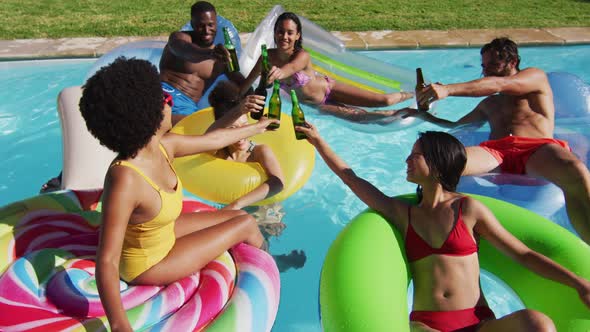 Diverse group of friends having fun playing on inflatables making a toast in swimming pool