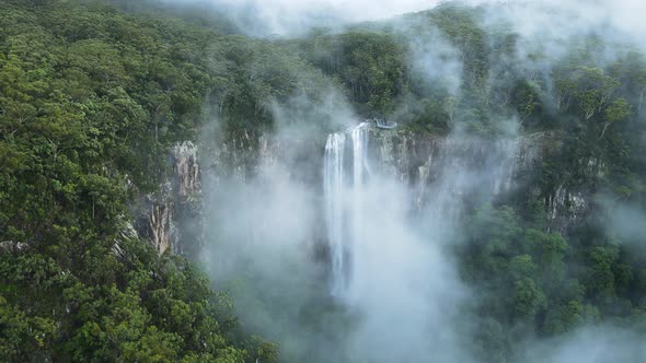 Unique view of a fog covered mountain revealing a majestic tropical waterfall lookout platform. Cine