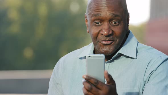 Elderly African American Man Holding Smartphone Looking at Screen During Video Chat Emotionally