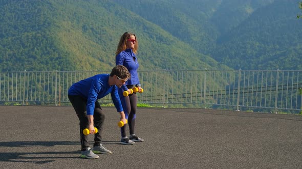 Bodybuilding Man and Woman Holding Dumbbells Outdoors