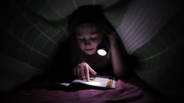 Little Child Girl Reading a Book with a Flashlight