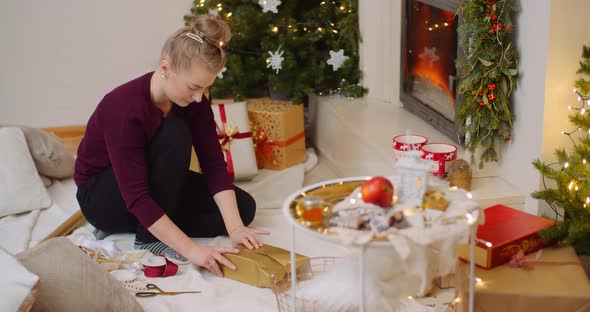 Woman Wrapping Christmas Present By Fireplace At Home