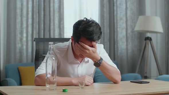 Drunk Asian Man With Smartphone On Table Crying And Pouring Vodka In A Shot Glass Before Drinking