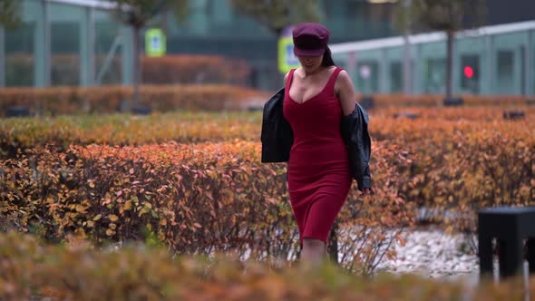 a Beautiful Business-like Confident Woman in a Purple Cap and Leather Jacket Strolls Along the City