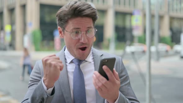 Middle Aged Businessman Celebrating on Smartphone, Outdoor