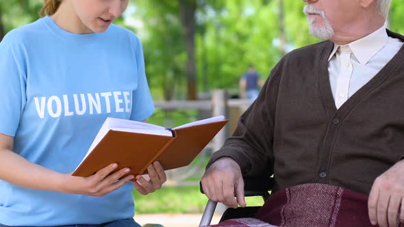 Sincere Social Worker Reading Book to Disabled Pensioner in Park, Volunteering