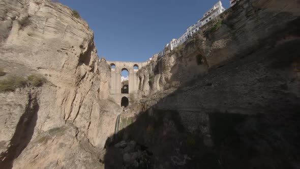 Slow aerial flight up deep gorge toward medieval arch bridge in Spain