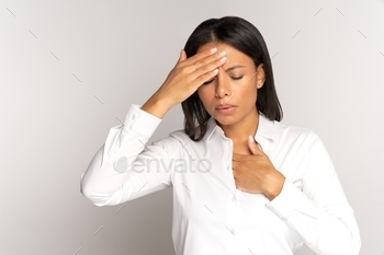 has covid-19 symptoms: breathing difficulties, fever and shortness of breath, isolated on gray background. Tired unhealthy mixed race woman with chest pain and headache suffer from migraine or stress, panic attack touching forehead