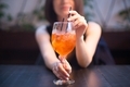 A young woman at the bar drinks an aperol cocktail from two tubes. Close-up dark photo. - PhotoDune Item for Sale